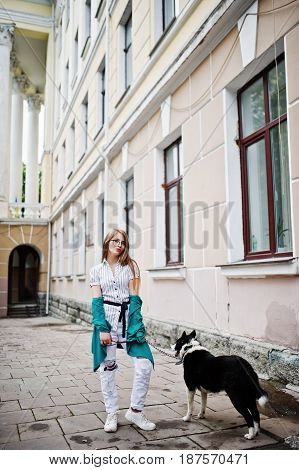 Trendy Girl At Glasses And Ripped Jeans With Russo-european Laika (husky) Dog On A Leash, Against St