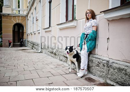 Trendy Girl At Glasses And Ripped Jeans With Russo-european Laika (husky) Dog On A Leash, Against St