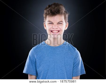Half-length emotional portrait of caucasian teen boy with blinking or closed eyes. Funny teenager wearing blue t-shirt on black background.