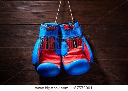 Boxing blue and red gloves hanging from ropes on a wooden background. Horizontal photo of the bright sportwear against brown wall. Boxing backgrounds and still-life. Concept of the active lifestyle.
