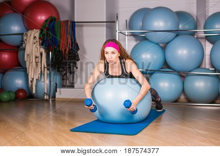 Woman exercising with dumbbells on a fitness ball.