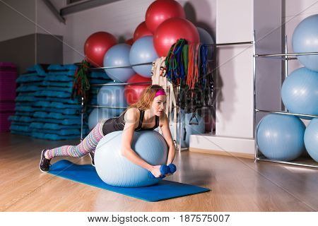 Woman exercising with dumbbells on a fitness ball.