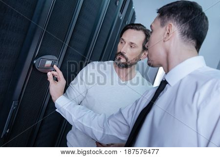 Limited access. Serious young male technician entering a code and pressing a button on the control panel while standing with his colleague