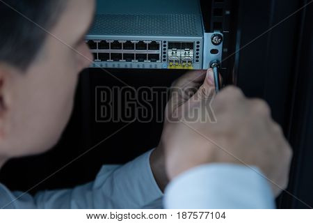 Repair service. Handsome experienced nice technician holding a screwdriver and putting it into a screw bolt while repairing a network server