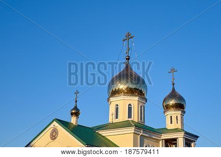 Eastern orthodox crosses on gold domes cupolas againts blue sky without clouds and green roofs