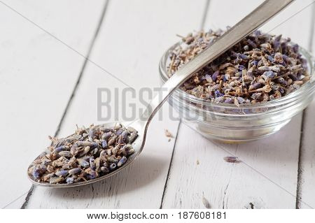 Lavender essential oil ingredients. Wooden spoon full of dry lavender seeds and bunch of dried lavender flowers with aromatherapy oil in small transparent bowl. Relaxing and calming body spa.