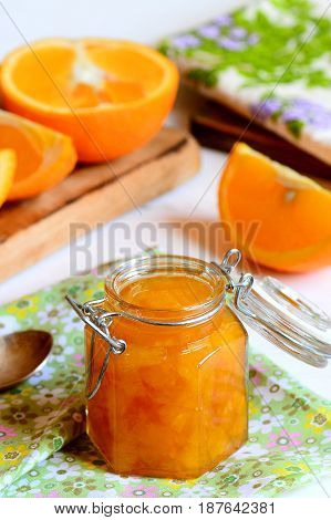 Citrus jam recipe to use up oranges. Homemade orange jam in a glass jar, textile napkin, orange slices on a table. Useful and sweet citrus dessert recipe