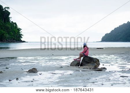 Woman Sitting On Rock Among Moist Sand Beach. Front Of Her Have Blue Sea,sky And Green Forest On Mou
