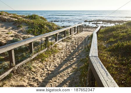 sandy walkway with wooden railings leading onto a tranquil beach at sunrise