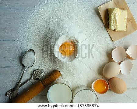Eggs flour milk sugar oil on a white wooden table.
