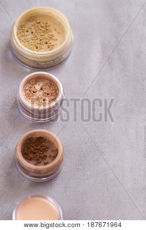 Mineral cosmetics beauty artist / blogger makeup kit loose powder bronzer concealer highlighter on gray concrete background. Top view. Copyspace
