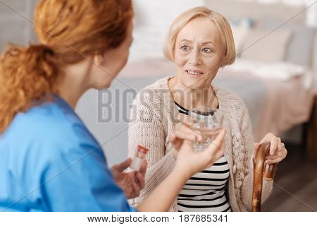 Two times per day. Feeble petite elderly lady receiving some help from a nurse who taking care of her and serving her a glass of water