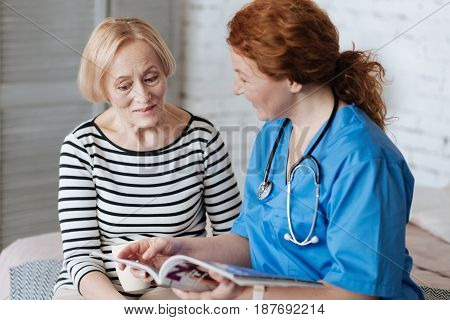 Valued attention. Friendly wonderful smart lady trying entertaining elderly lady while paying her a visit and assigning her with the recovery