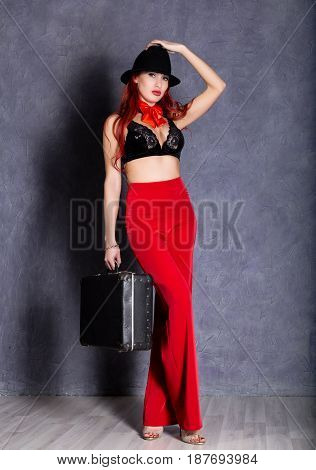 woman in red pants and black hat with big boobs hold retro suitcase.