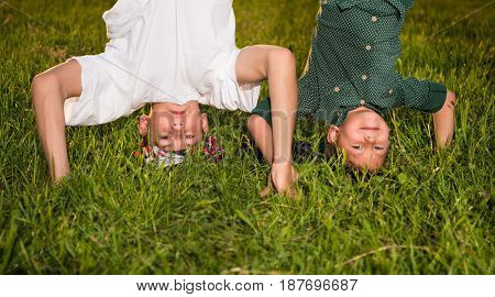 Happy Children Standing Upside Down On Green Grass