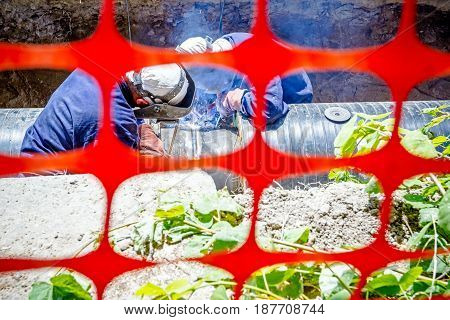 Welders are in trench they arc welding pipeline. Confined space with orange plastic safety net