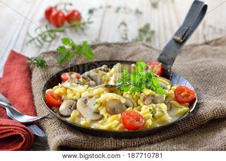 Vegetarian Swabian spaetzle with thickened cream sauce and fresh mushrooms served in an iron frying pan on a rustic table with an old jute sack