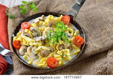 Vegetarian Swabian spaetzle with thickened cream sauce and fresh mushrooms served in an iron frying pan on a rustic table with an old jute sack