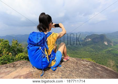 successful woman hiker taking photo with cellphone hiking on mountain peak