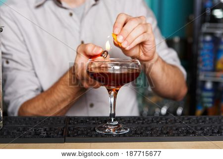 Barman's hands in bar interior making alcohol flaming cocktail. Professional bartender at work in bar mixing drink with burning fire. Party time in night club