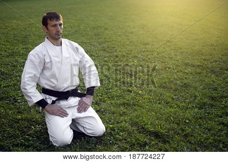 Ninja in white kimono is sitting on the grass outdoors and resting.