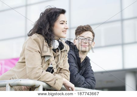Two smiling teenagers standing leaning on the railing and talk