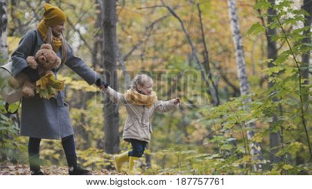 Little daughter with her mommy and Taddy bear walks in autumn park - plays the leaves, telephoto