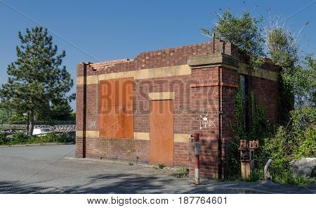 An abandoned and boarded up brick gate house near a factory