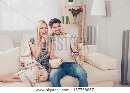 Young Beautiful Couple Of Blondie And Brunette Guy Are Watching Movie Under The Beige Plaid, Eating