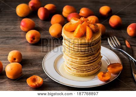 Stack of homemade american pancakes served with honey and apricots on wooden background.