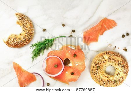 Bagel ingredients. Lox, purple onions, capers, dill, and the buns, shot from above on a white marble background in the process of making, with a place for text