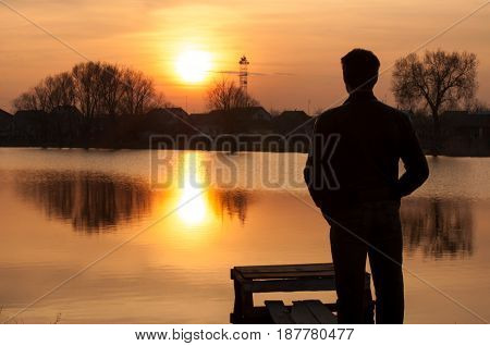 Man silhouette standing on river stones gangway and contemplating a beautiful sunset.