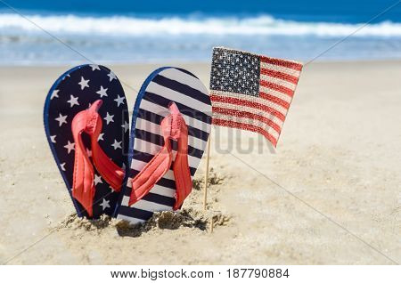 Patriotic USA background with flip flops and American flag on the sandy beach