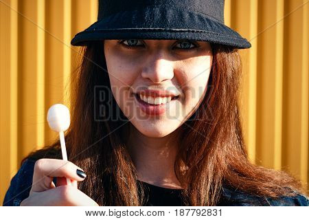 Cheerful Stylish Young Girl In Hat, And Jeans Jacket With Candy On Stick, Chupa Chups, On Sunny Day