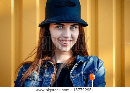 Cheerful Stylish Young Girl In Hat, And Jeans Jacket With Candy On Stick, Chupa Chups, On Sunny Day