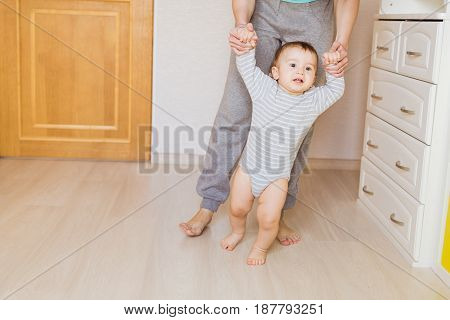 Cute boy taking first steps holding mums hands
