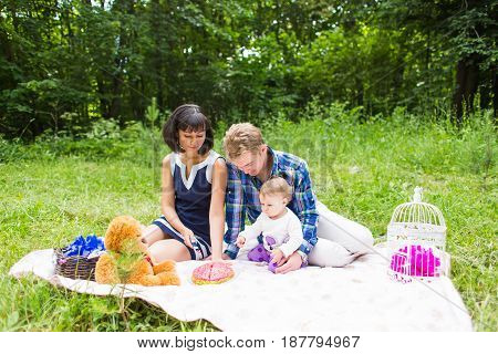 Happy young mother and father with their baby daughter relaxing on a blanket in a park celebrating with birthday cake.