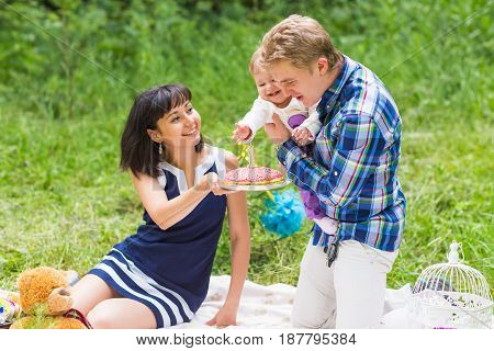 Happy young mother and father with their baby daughter relaxing on a blanket in a park celebrating with birthday cake.