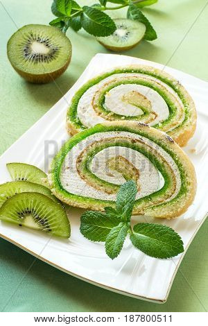 Delicious cake roll with kiwi marmalade and marshmallow. Sliced rolls on a plate fresh kiwi and mint. Tasty fruit dessert. Vertical