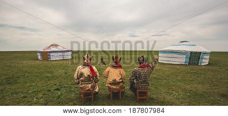 Three Kalmyk musicians in national costumes in the steppe against the background of yurts, the spring steppe. Russia