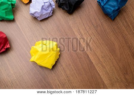 Top View Of Yellow Crumpled Paper Ball On Dark Brown Wood Table With Group Of Colorful Crumpled Pape