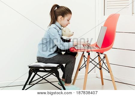 Little Girl Typing On Laptop With Teddy Bear Toy