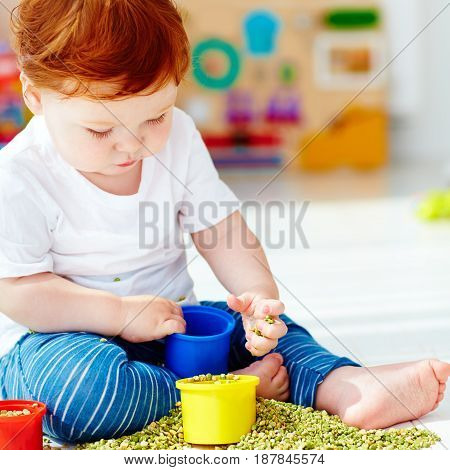 Cute Redhead Baby Boy Developing His Fine Motility Skills By Playing With Green Peas At Home