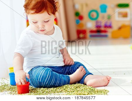 Cute Redhead Baby Boy Developing His Fine Motility Skills By Playing With Green Peas At Home