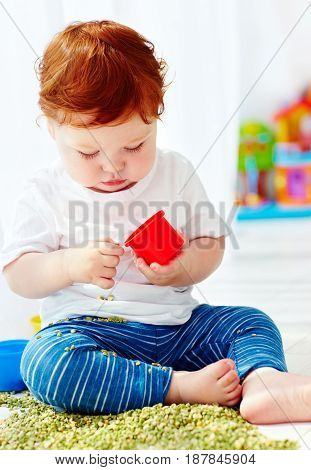 Cute Redhead Baby Boy Developing Fine Motility Skills By Playing With Green Peas At Home