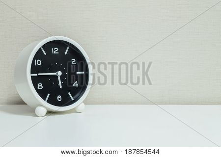 Closeup black and white alarm clock for decorate in a quarter to six o'clock or 5:45 p.m. on white wood desk and cream wallpaper textured background with copy space