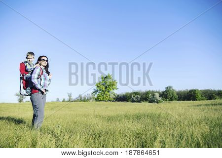 Mother with baby in backpack carrier is hiking in mountains. Tourist is carrying a child on his back on the nature.
