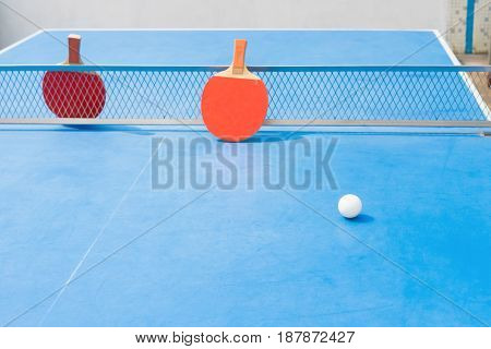 pingpong rackets and ball and net on a blue pingpong table