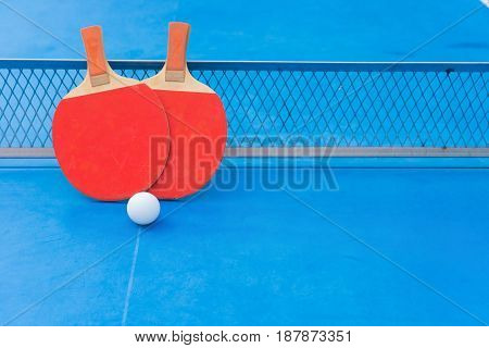 two pingpong rackets and ball and net on a blue pingpong table with copy space