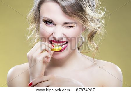 Portrait of Sexy Caucasian Blond Girl Eating Tiny Lemon Piece. Demonstrating Too Much of Acid Taste Of the Fruit. Against Yellow Background.Horizontal Image Orientation